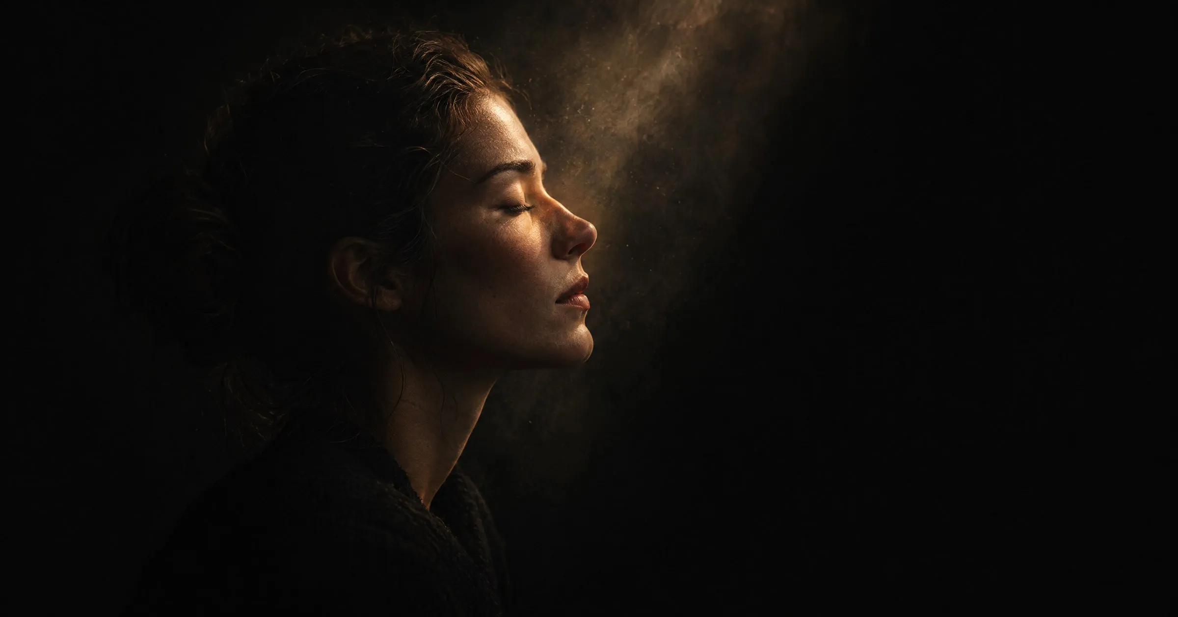 A woman in profile with eyes closed, lit by a soft beam of light